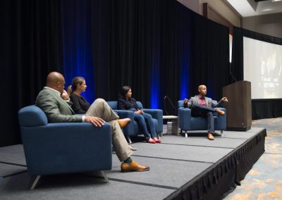 Four people sit on stage in a panel discussion, with one person speaking into a microphone.
