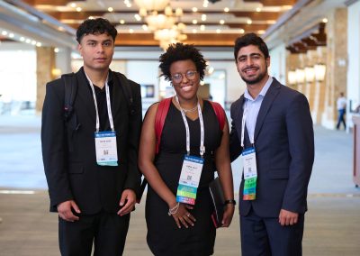 Three people in formal attire stand together in a conference hallway, wearing name tags and lanyards.