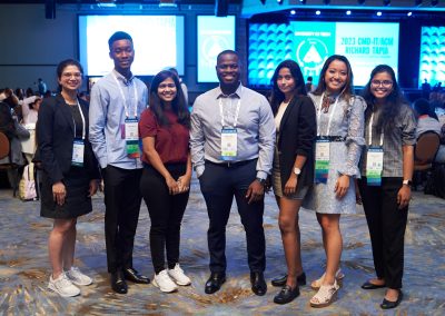 Group of seven people standing in a row, smiling, in front of a conference stage with "2023 CMD-IT/ACM Richard Tapia" on the screens.