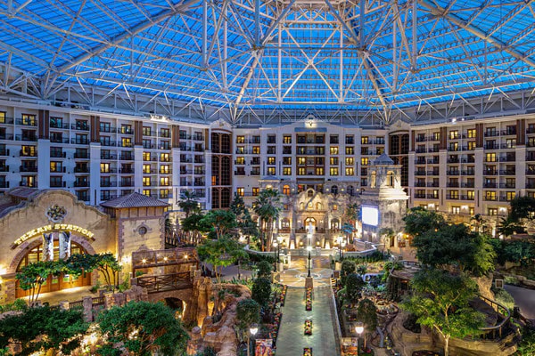 The spacious glass-ceiling atrium serves as a stunning venue for tapia, with multiple floors showcasing a central garden area, serene water features, and numerous balconies overlooking the enchanting interior space.